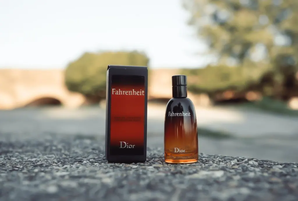 عطر مردانه ادو تویلت Fahrenheit از برند دیور در فضای باز در کنار جعبه عطر به رنگ مشکی و قهوه‌ای و نام عطر